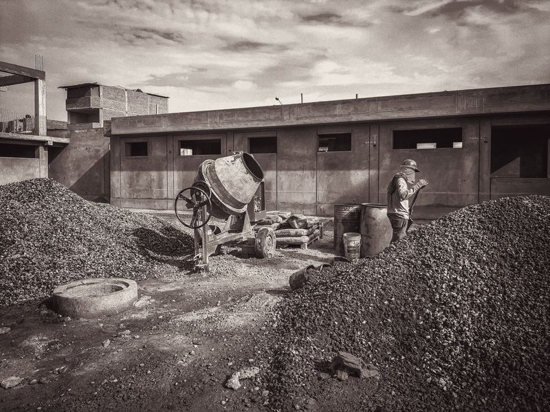 Canteiro de obras com betoneira e estrutura de concreto em execução ao fundo.